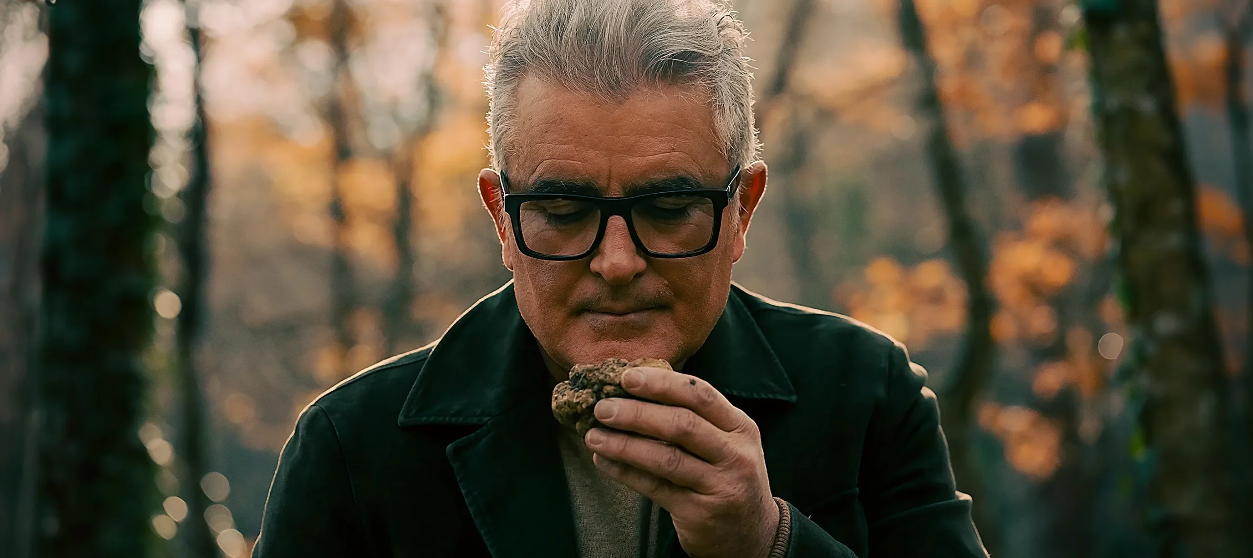 Giuliano Martinelli e l’autentico profumo del tartufo Giuliano Martinelli, nel bosco, che avvicina al viso un tartufo appena raccolto per sentirne l'aroma intenso e la qualità.