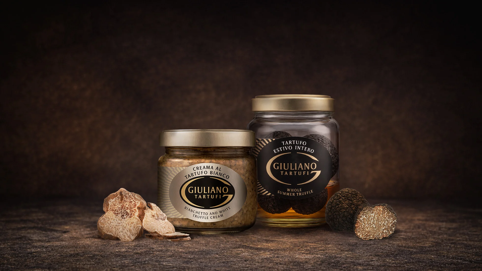 Due barattoli in vetro di specialità al tartufo Giuliano Tartufi accanto a tartufi interi freschi, a sottolineare l'autenticità degli ingredienti.